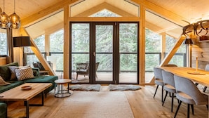 A spacious loft-style room with a high ceiling, large windows, a dining area, and a cozy seating area. - Lavish chalet with sauna & hot tub (Turrach)