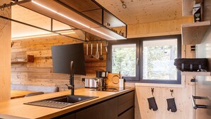 A modern kitchen with wooden walls, a large window, and a built-in oven. - Lavish chalet with sauna & hot tub (Turrach)