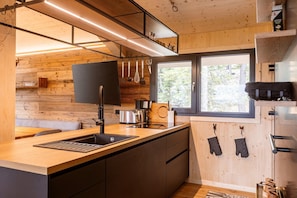 A modern kitchen with wooden walls, a large window, and a built-in oven. - Lavish chalet with sauna & hot tub (Turrach)