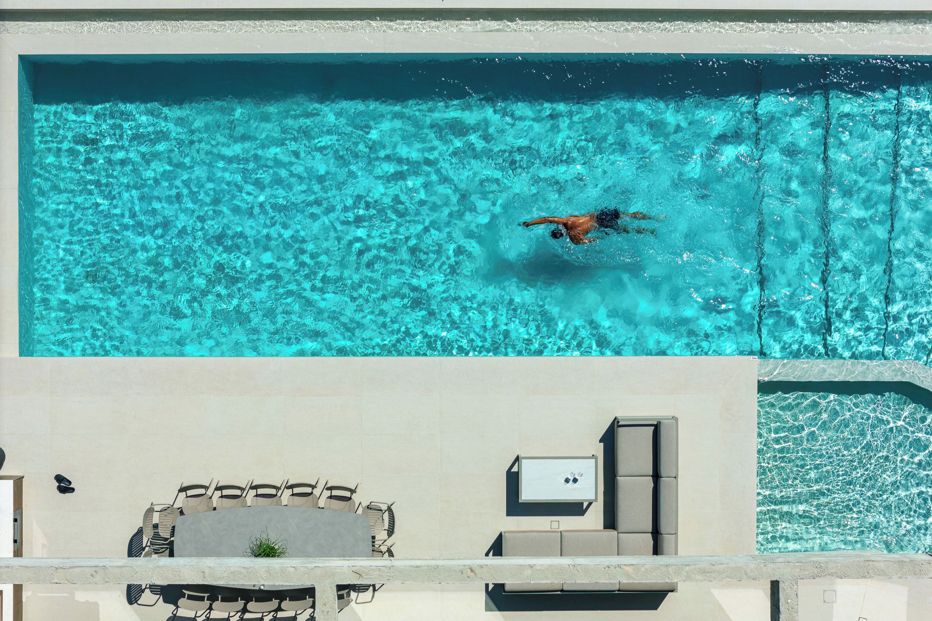 A swimming pool with clear blue water, a lounge area with chairs and a table, and a small plant.