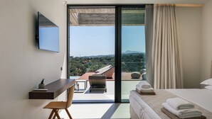 Ein modernes Hotelzimmer mit einer großen Glaswand, die auf einen Balkon führt, einem Bett mit ordentlich gefalteten Handtüchern, einem Schreibtisch mit Stuhl und einem an der Wand befestigten Flachbildfernseher.