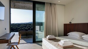 Ein modernes Hotelzimmer mit einer großen Schiebeglasdoor zum Balkon, einem ordentlich bezogenen Bett, einem Schreibtisch mit Stuhl und Blick auf die Landschaft.