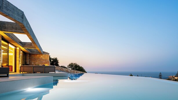 Ein moderner Infinity-Pool mit freiem Blick auf den Ozean, einer Steinfassade und einer integrierten Sitzgruppe.