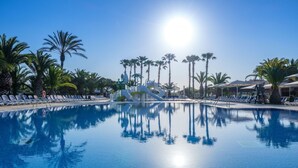 A clear blue pool with a water slide, surrounded by palm trees and lounge chairs. - Charming Getaway with Garden (Tarragona)