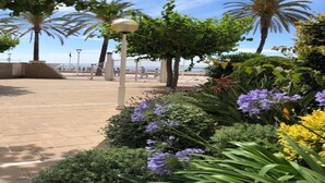 A paved walkway with palm trees and flowering plants, leading to a beach area. - Charming Getaway with Garden (Tarragona)