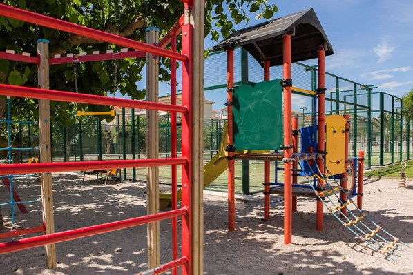 Un parc infantil amb una estructura per escalar, tobogan i zona de jocs coberta.