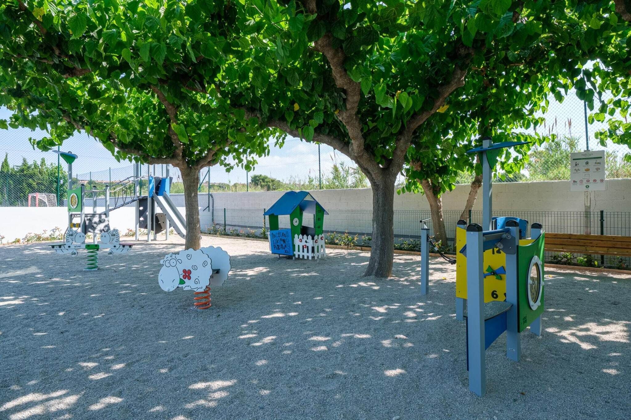 Une aire de jeux dotée de diverses structures ludiques, notamment un toboggan et des jeux d’escalade, le tout à l’ombre des arbres.