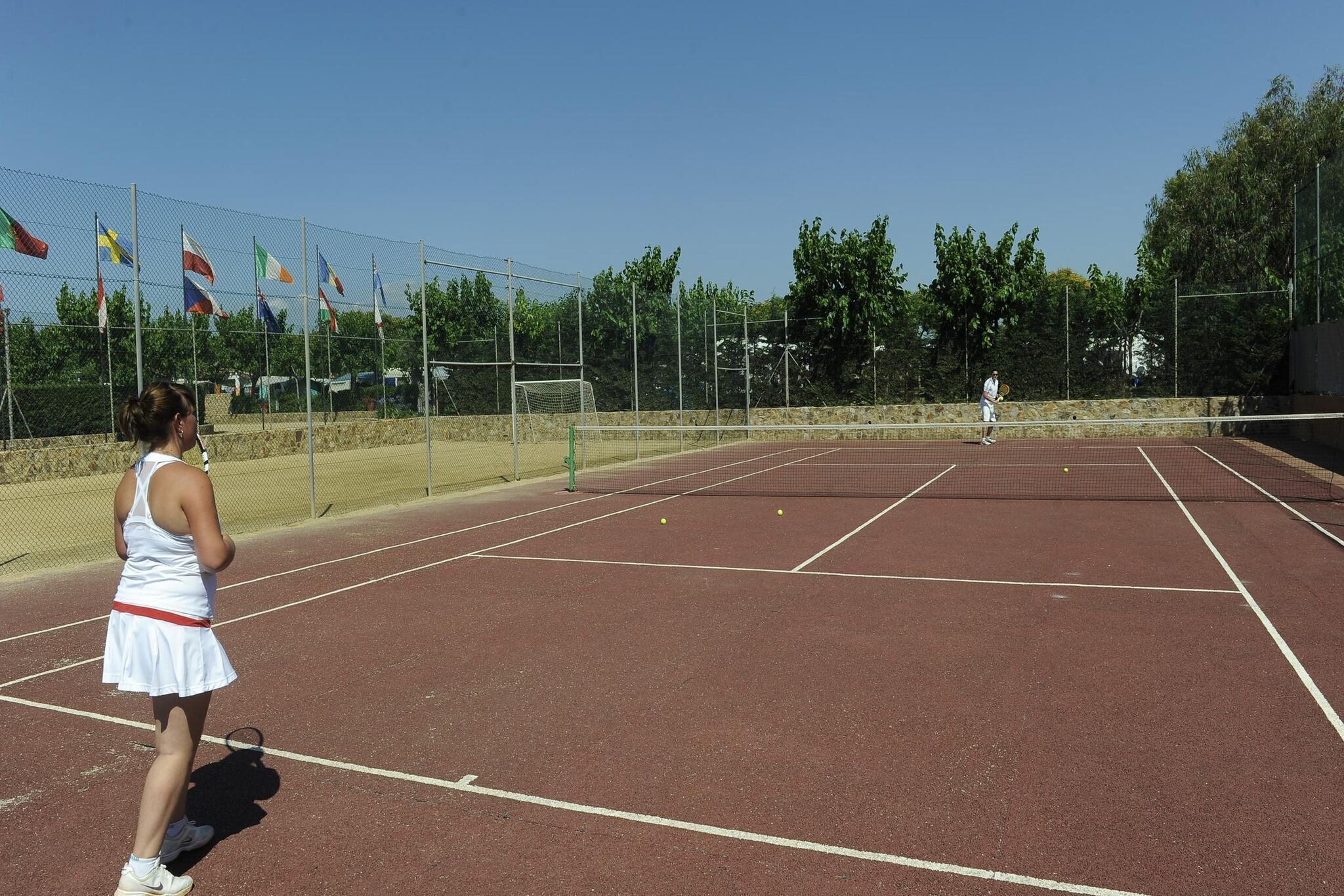 A tennis court with a net, flags, and a player in the background.