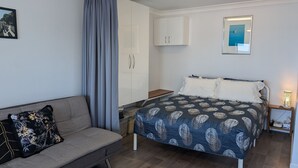 A bedroom with a bed, a sofa, a wardrobe, and a nightstand with a lamp.