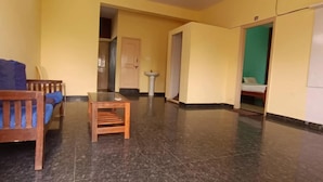 Een kamer met een houten bank, een kleine houten tafel, een betegelde vloer, een wastafel en een bed tegen een groene wand.