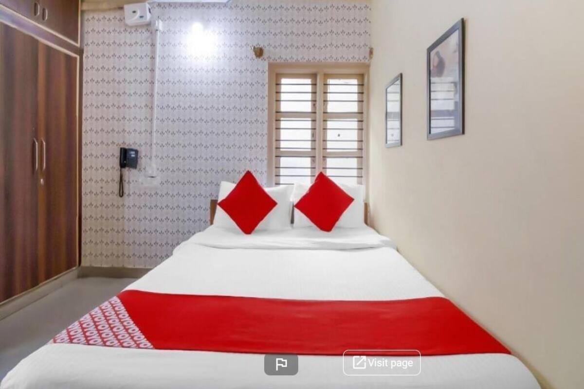 A hotel room with a bed, a wardrobe, an air conditioning unit, and a window with blinds.