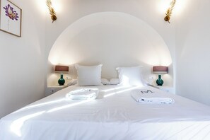 Cama bem arrumada com lençóis e toalhas brancas, duas luminárias de cabeceira e um quadro na parede.