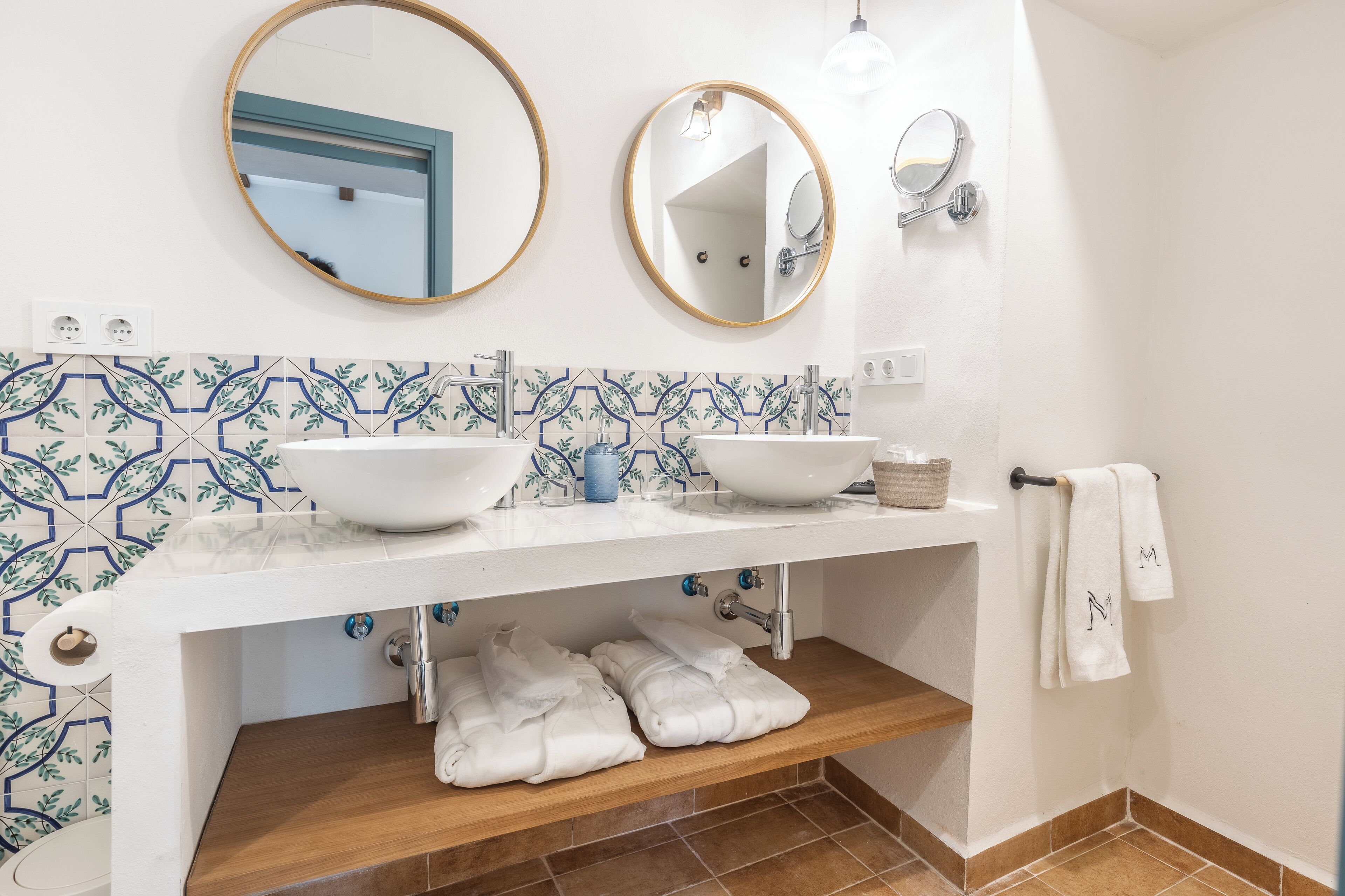 A bathroom with two sinks, a mirror, a towel rack, and a shelf with towels.