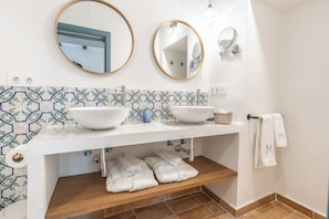 A bathroom with two sinks, a mirror, a towel rack, and a shelf with towels. - Hospedium Hotel Rural Virgen María (Guillena)