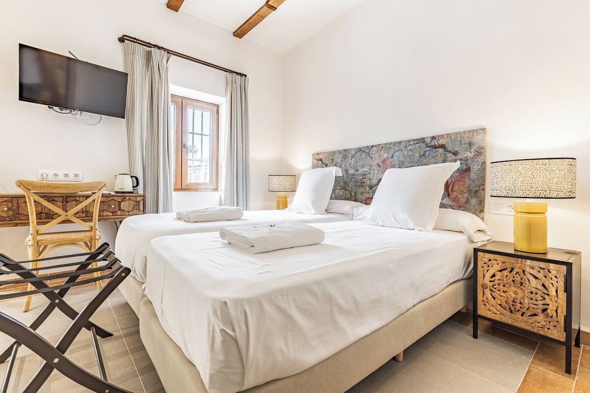 A hotel room with two beds, a flat-screen TV, a desk with a chair, and a window with curtains.