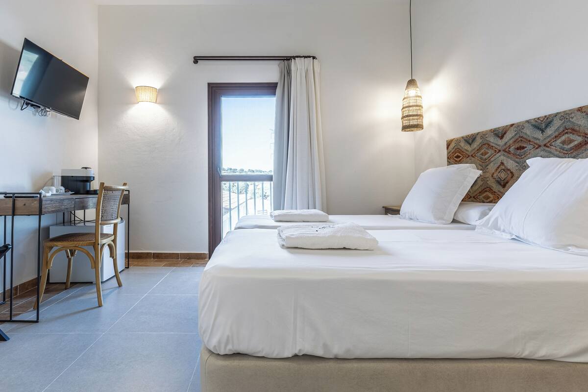 A hotel room with a bed, a desk with a chair, a television, and a window with curtains.
