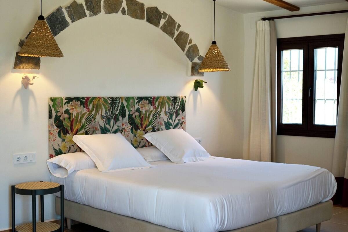 A bed with white bedding, two hanging lamps, a stone arch, and a window with curtains.