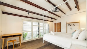Une chambre avec un bureau en bois, un lit avec une literie blanche et une fenêtre avec des stores.