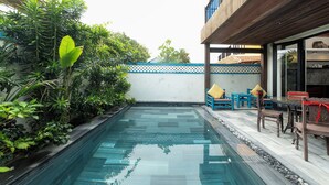 Une piscine dotée d’une terrasse en bois, entourée d’une végétation luxuriante et d’une clôture blanche.