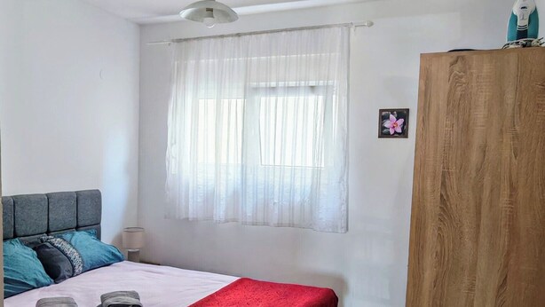 A bedroom with a bed, a wooden wardrobe, a ceiling fan, and a window with sheer curtains. - Stan Julietta - With a Boka Bay View Ground Floor With a Residential Parking (Ðenovici)