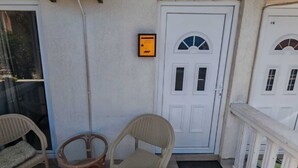 A porch with two wicker chairs, a white door with a window, and a small yellow device on the wall. - Stan Julietta - With a Boka Bay View Ground Floor With a Residential Parking (Ðenovici)