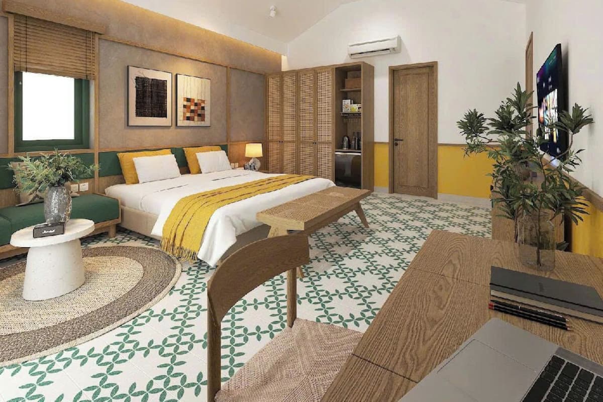 Ein modernes Hotelzimmer mit einem großen Bett, einem Schreibtisch mit einem Laptop, einem grünen Sofa und einer Zimmerpflanze.