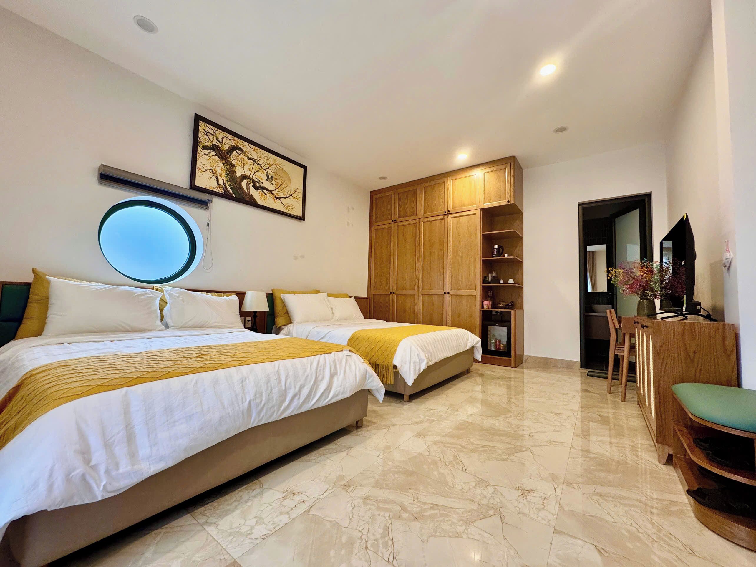 Una habitación de hotel con dos camas, un armario de madera, un espejo redondo y un pequeño escritorio con una silla.