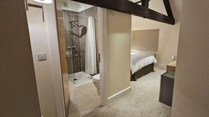 Une chambre à coucher comprenant un lit, une table de chevet et un espace douche doté d’une porte en verre.