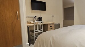 Une chambre comprenant un lit, un bureau avec une chaise, un téléviseur fixé au mur et un petit coin cuisine.