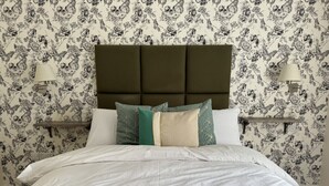 A neatly made bed with a green throw blanket, a brown upholstered headboard, and a floral wallpaper pattern. - Class Stays - Room 2 (Shrewsbury)
