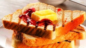 Deux tranches de pain grillé, beurrées et garnies de confiture, sur une assiette blanche.