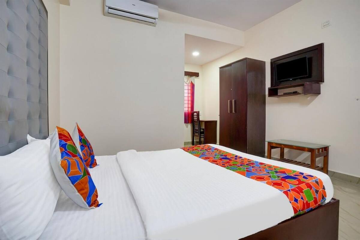 Quarto de hotel com uma cama, televisão fixada na parede e uma escrivaninha.