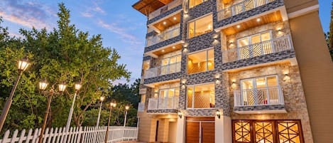 A multi-story hotel with balconies, a white picket fence, and a paved driveway.