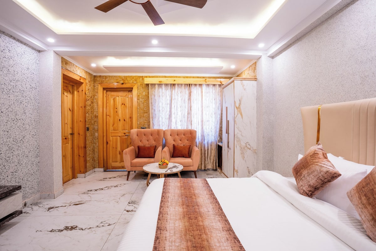 Habitación de hotel con cama, zona de estar con dos sillones, una mesita con frutero y un ventilador de techo.