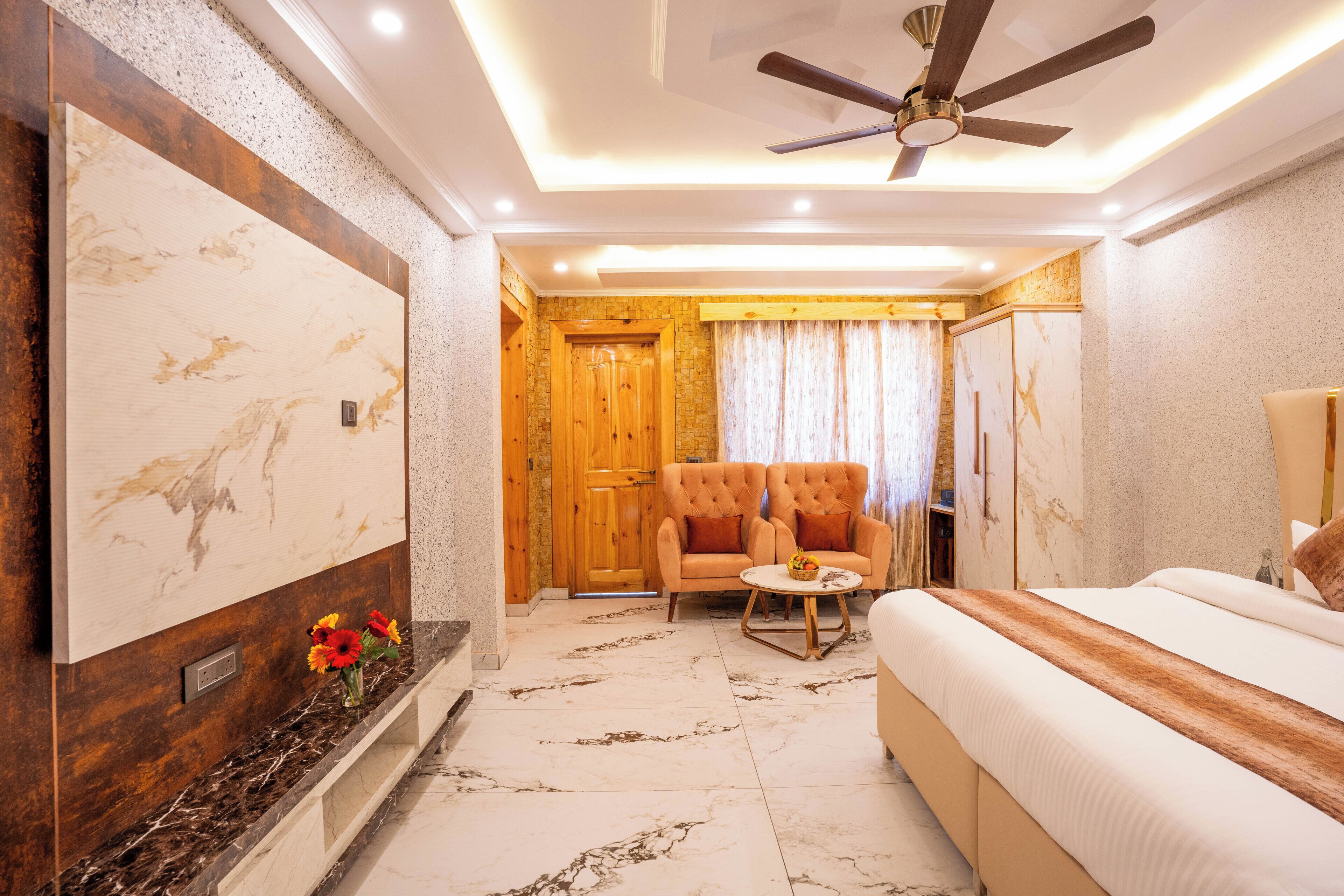 A hotel room with a marble floor, a bed, a sofa, a chair, a ceiling fan, and a large wall-mounted TV.