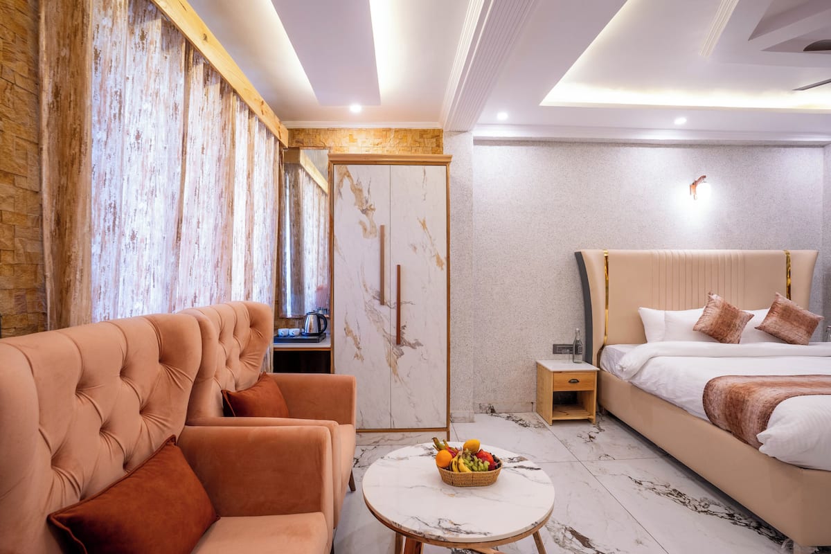 Una habitación de hotel moderna con un sofá cómodo, una cama con cabecera de mármol, una mesita redonda con fruta y una puerta de madera.