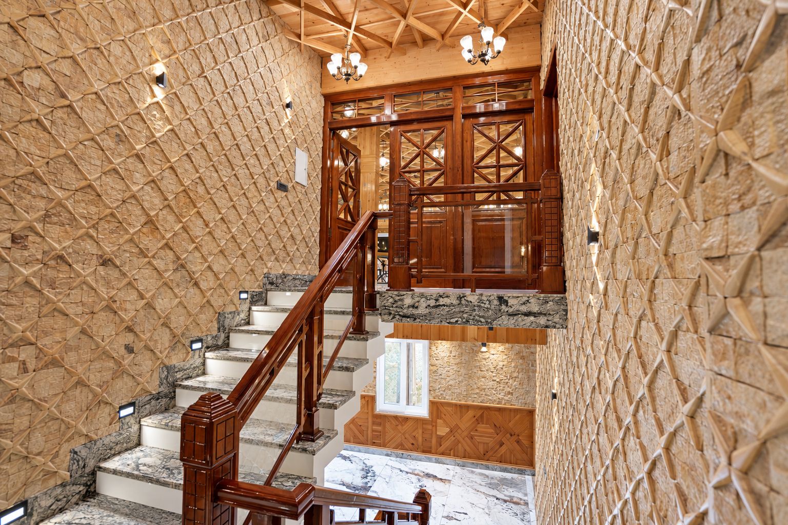 Una escalera con barandillas de madera y peldaños de mármol, que conduce a una habitación con paneles de madera y un candelabro.