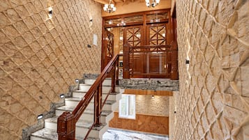 Una escalera con barandillas de madera y peldaños de mármol, que conduce a una habitación con paneles de madera y un candelabro.