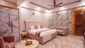 A bedroom with a marble floor, a bed with a tufted headboard, a pink sofa, a round table with fruit, and a wooden door.