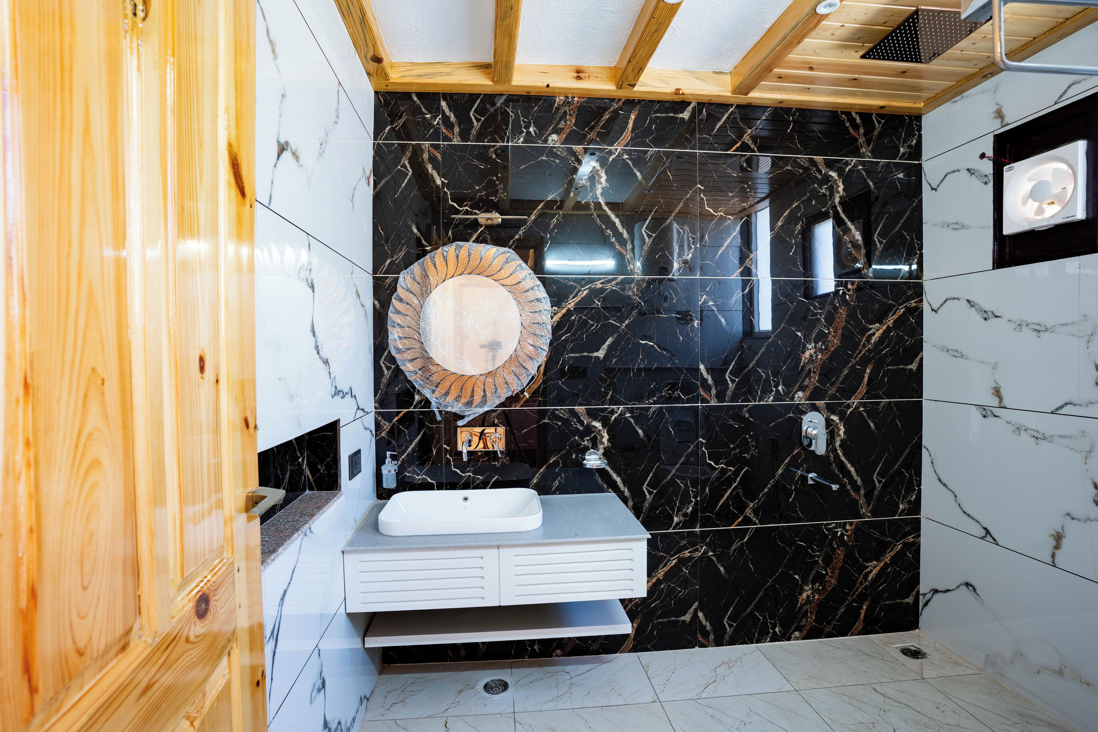 Un baño moderno con tocador de madera, lavamanos blanco y salpicadero de mármol negro.