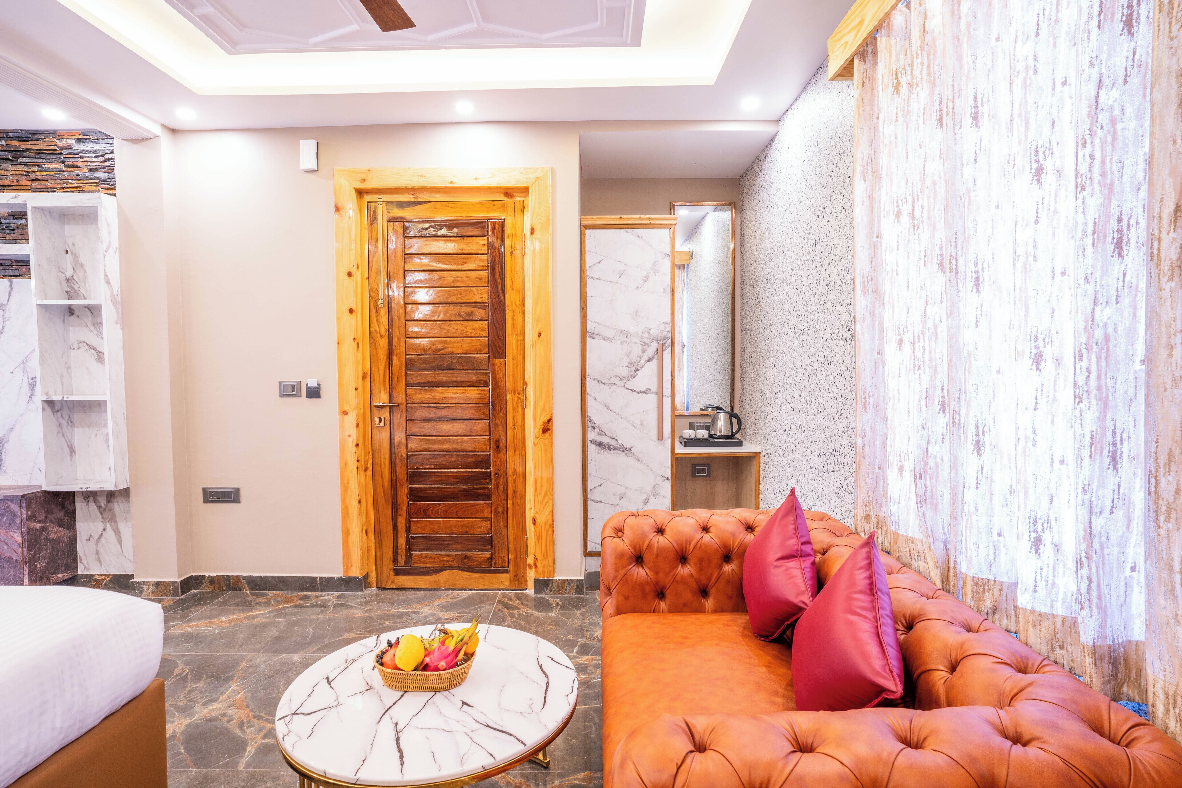 A modern hotel room with a marble floor, a wooden door, a plush orange sofa, and a marble coffee table with fruit.