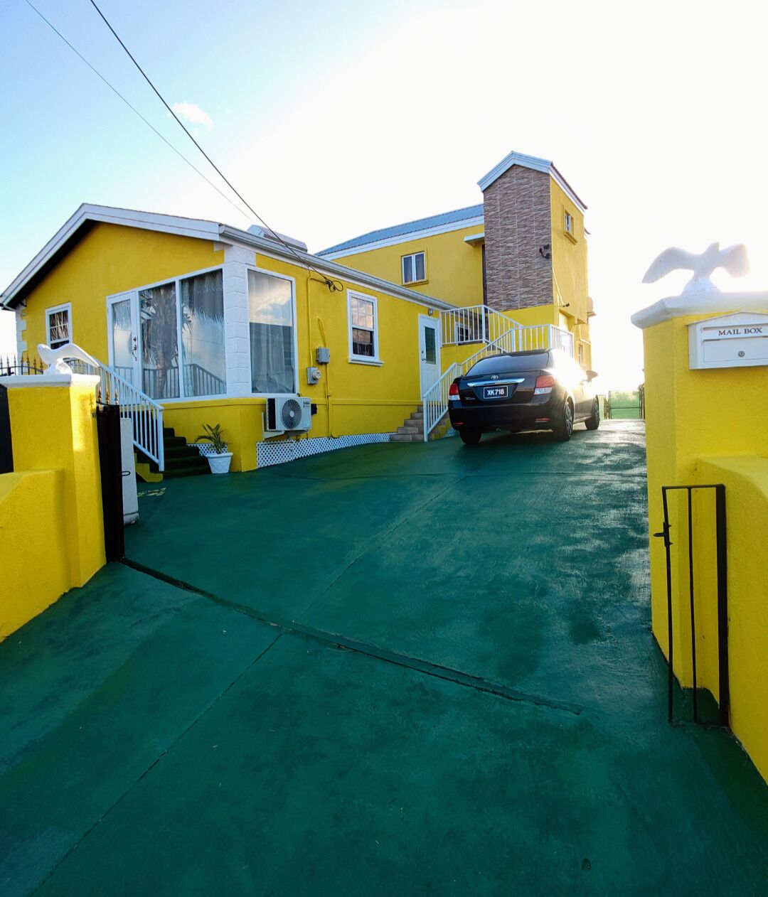A yellow building with a mailbox, a staircase, and a car parked in front.