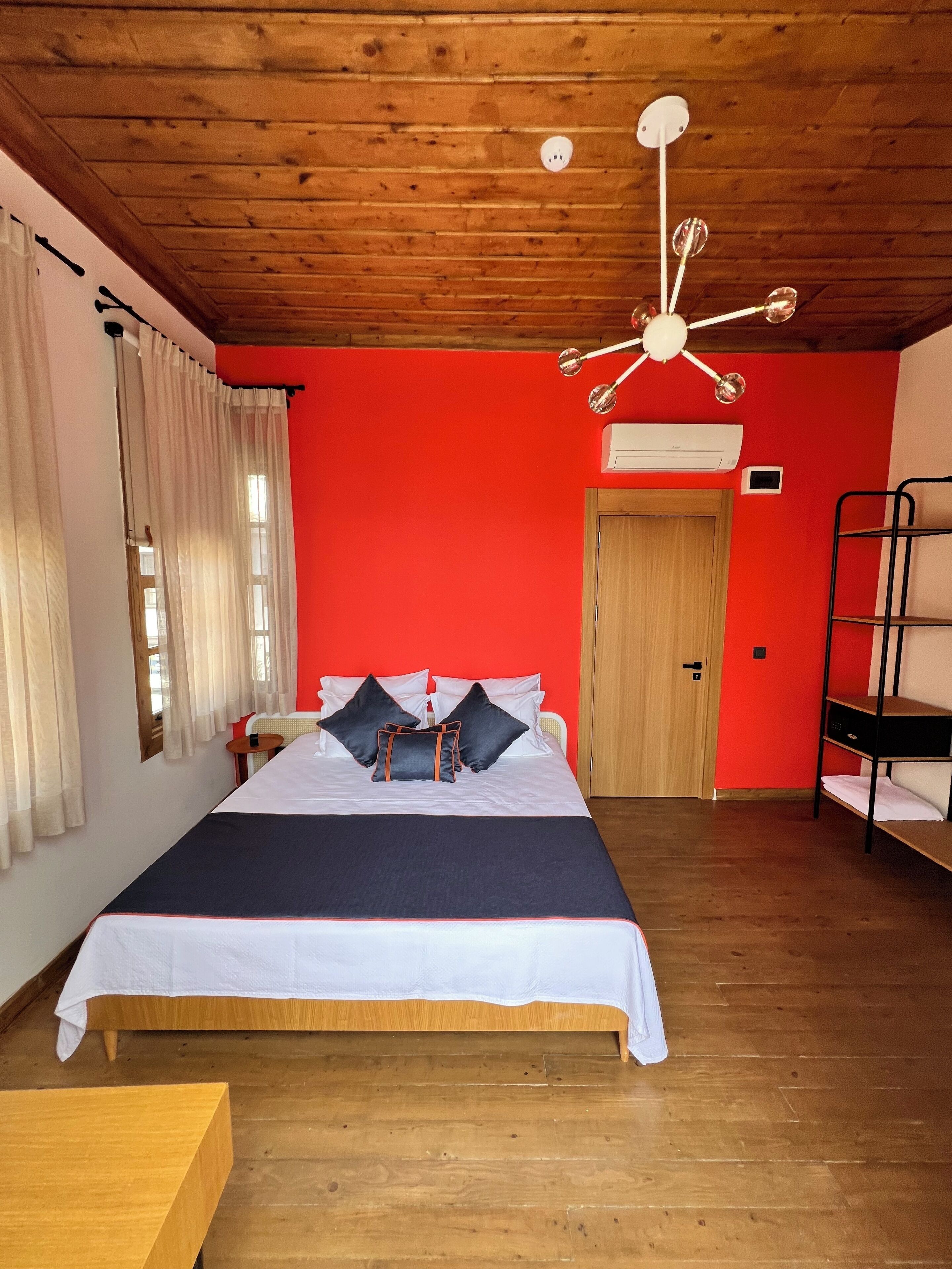 Ein Zimmer mit Holzboden, einem Bett mit weißer Bettwäsche, einer roten Wand und einem Etagenbett.