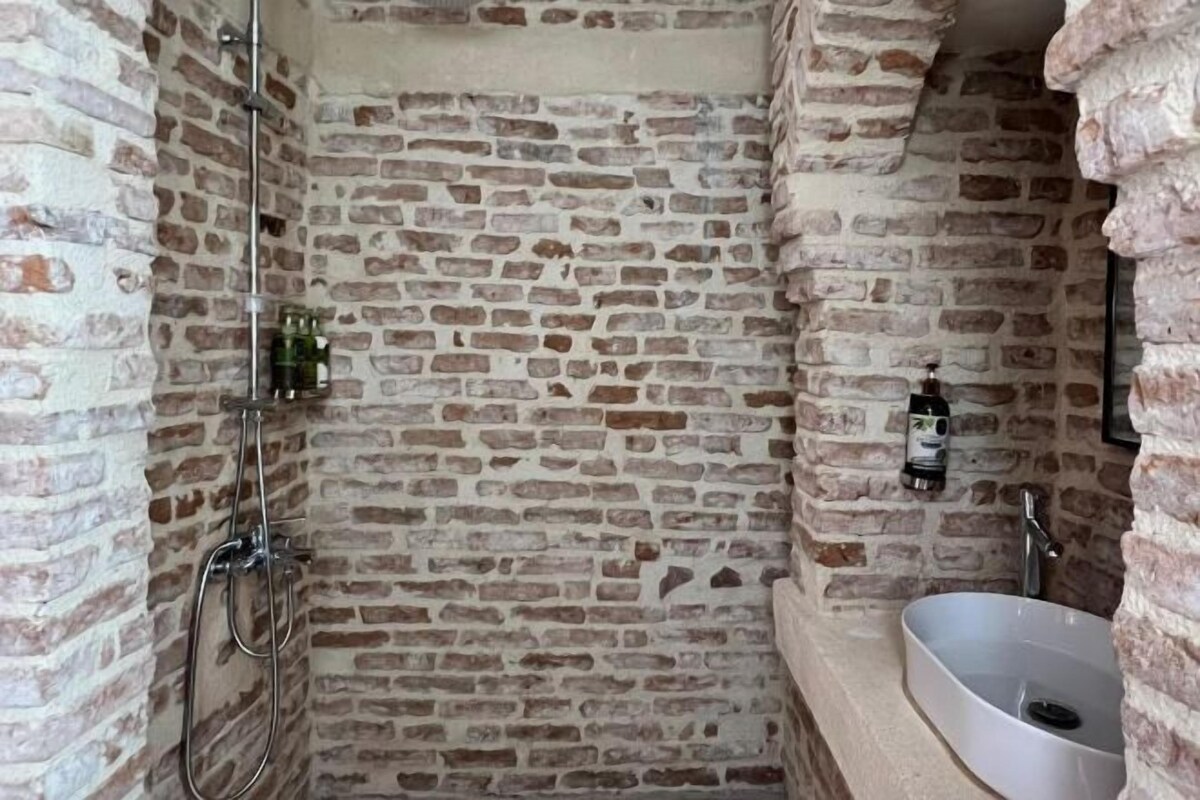 Ein Badezimmer mit Steinwänden, einer Dusche, einem Waschbecken und einem Spiegel.
