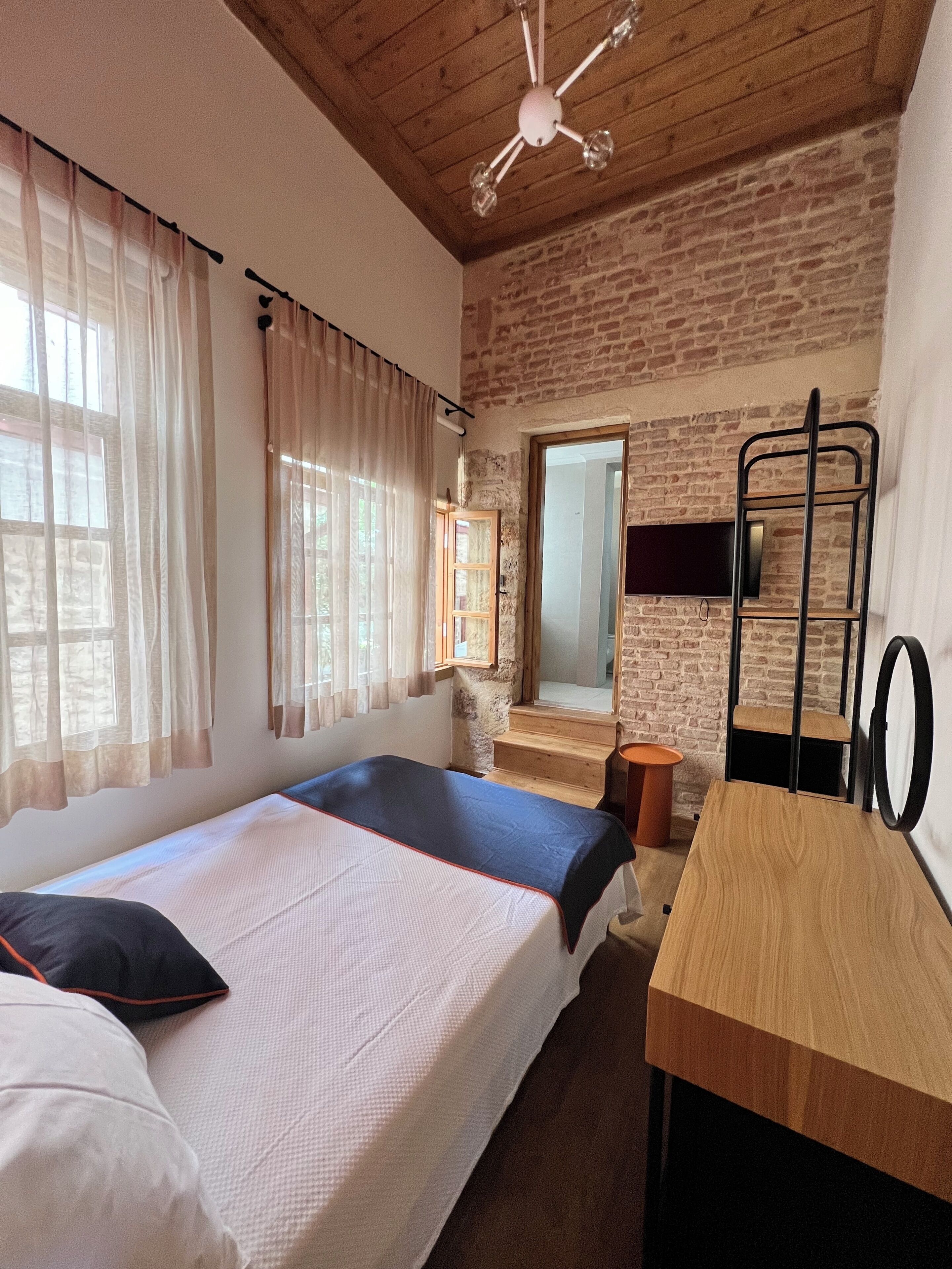 Ein Zimmer mit zwei Betten, einem Holztisch, einem Fernseher und einer Ziegelwand.