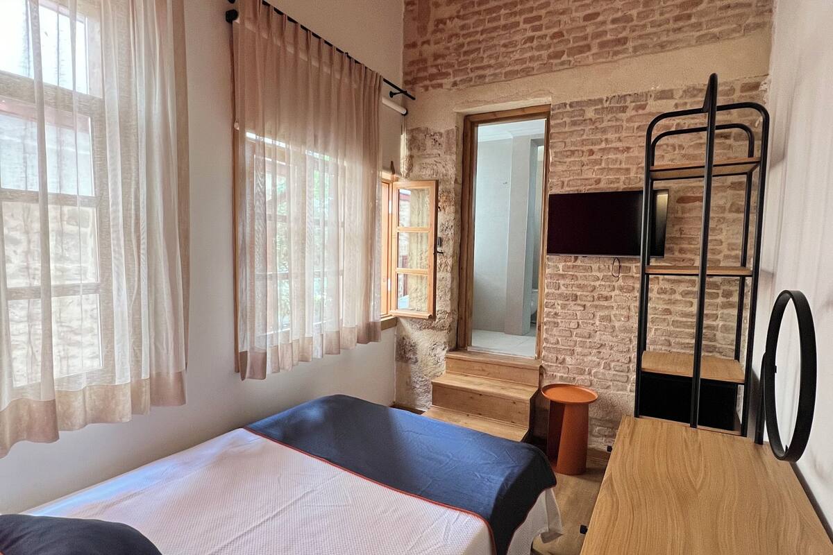 A room with two beds, a wooden desk, a mirror, a TV, and a brick wall.