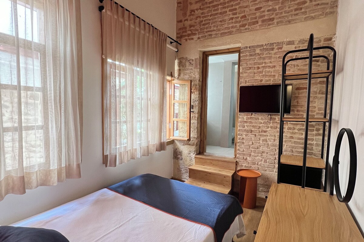 A room with two beds, a wooden desk, a mirror, a TV, and a brick wall.