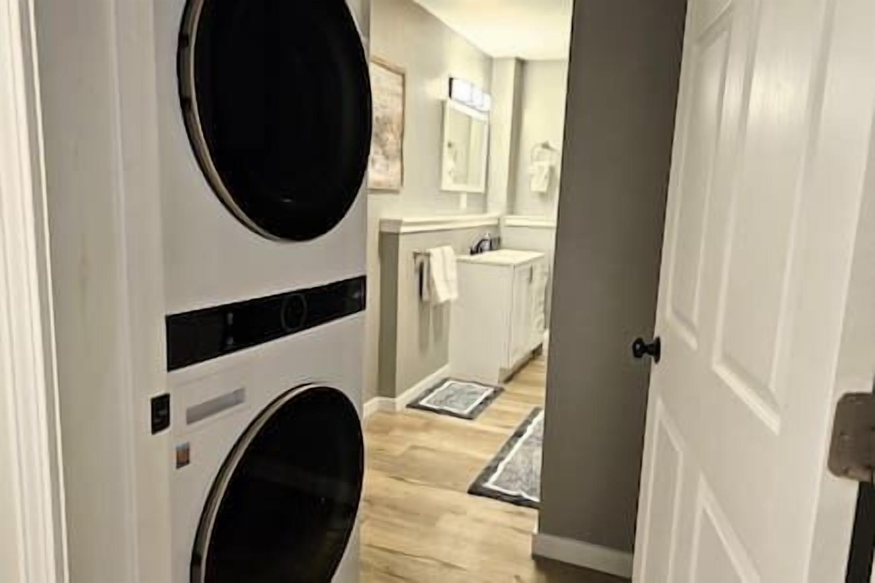 A laundry room with stacked washers and dryers, a sink, and a mirror.