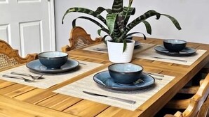 A wooden dining table with two bowls and a spoon on placemats, a potted plant, and a chair.