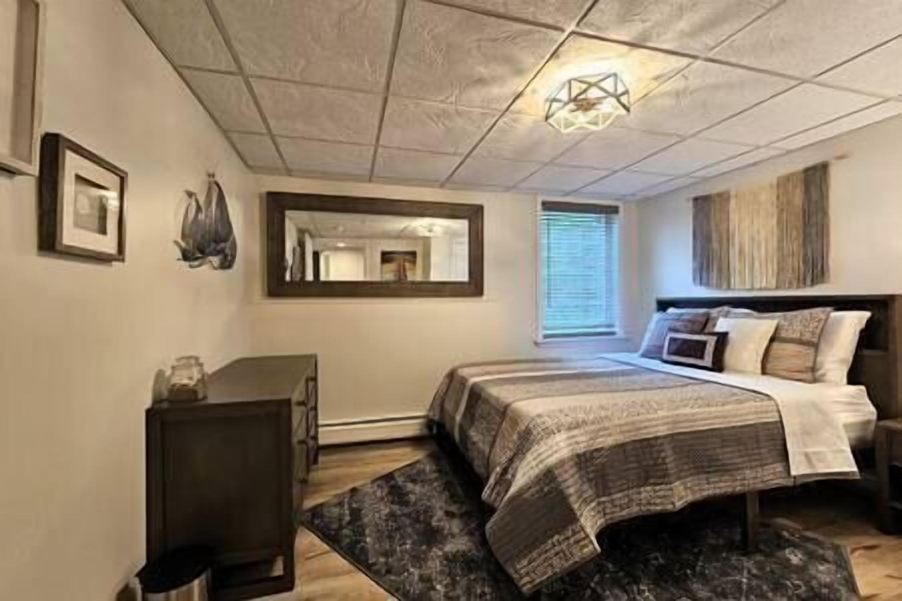 A bedroom with a bed, bedside table, dresser, and a large mirror.